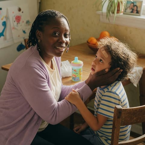 A gentle caregiver calmly reassuring a young child with a warm smile at home